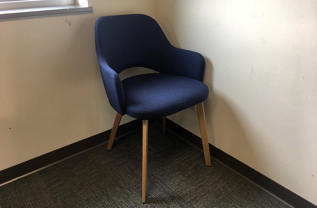 Granatowe krzesło biurowe źle ustawione w kącie, ilustrujące błędy w aranżacji przestrzeni biurowej.